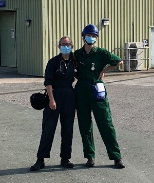 Phoebe stands smiling with another student outside the equine hospital. They are both wearing clinical clothing with stethoscopes and equipment
