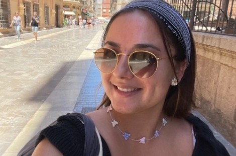 Malini is standing in a Spanish street, wearing sunglasses and smiling.